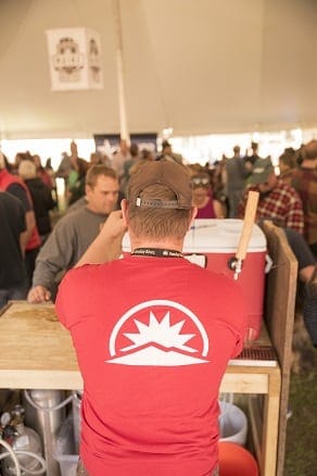 Staff wearing a Sunday River Red shirt pours a beer for a guest under the tent at Sunday Rivers Brew Fest 