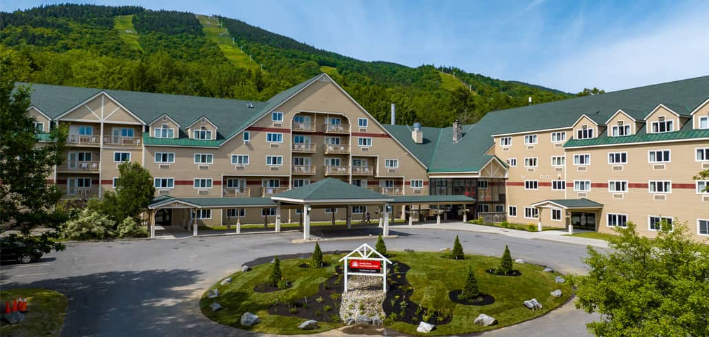 A view of the Grand Summit Hotel's entrance in the summer with the slopes of White Cap in the distance 