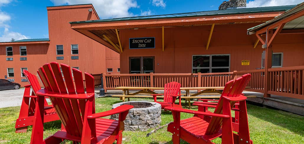 Red adirondack chairs encircle a firepit in front of the Snow Cap Inn's entrance on a beautiful summer day