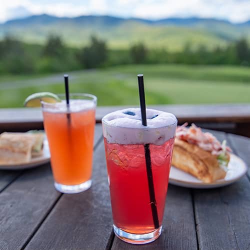 Two brightly colored cocktails and sandwiches on the Club House Deck on a sunny summer day 